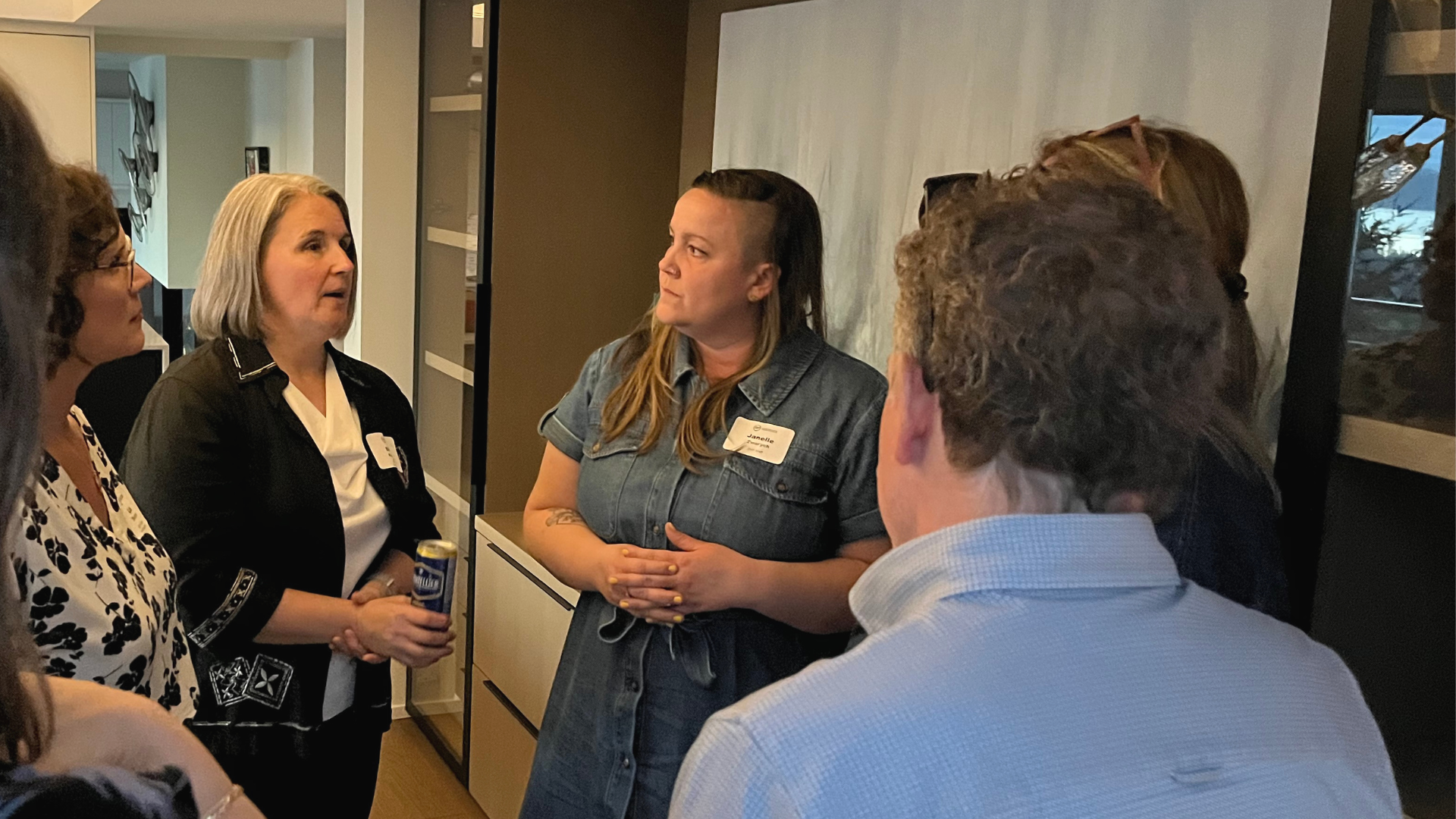 Colleagues gather listening intently to women to short grey hair in a house setting